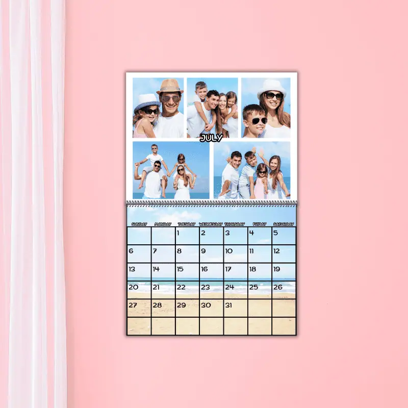 a photo calendar hanging on a pink wall with a sheer white curtain next to it. The calendar is set to July 2025. The top portion of the calendar has photos of a family at the beach and the bottom portion has the background of a beach and the days in front