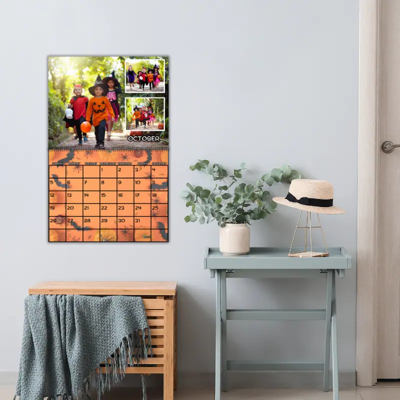 A photo calendar hanging on the wall near the entry way. The month is set to October 2025. The top portion has photos of children trick or treating and the bottom has a Halloween themed background with the dates on top.